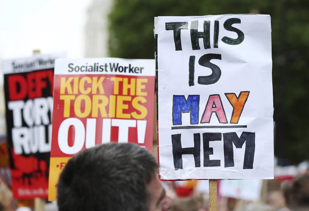People hold up placards against the Conservative government as they gather in Whitehall, to protest after the fire at Grenfell Tower which engulfed the 24 storey building on Wednesday, in London, ...
