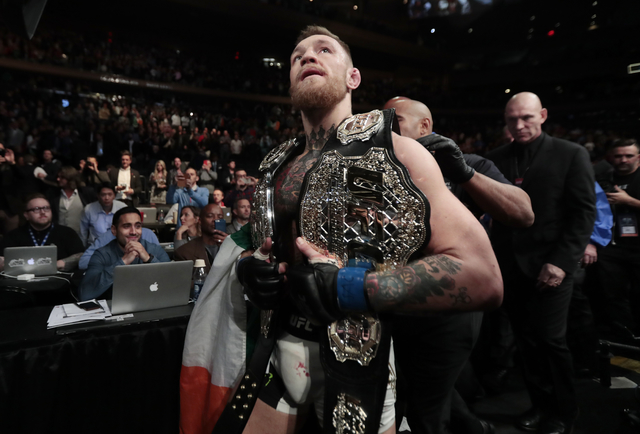 Conor McGregor leaves the octagon with his title belts after knocking out Eddie Alvarez during a lightweight mixed martial arts bout at UFC 205, early Sunday, Nov. 13, 2016, at Madison Square Gard ...