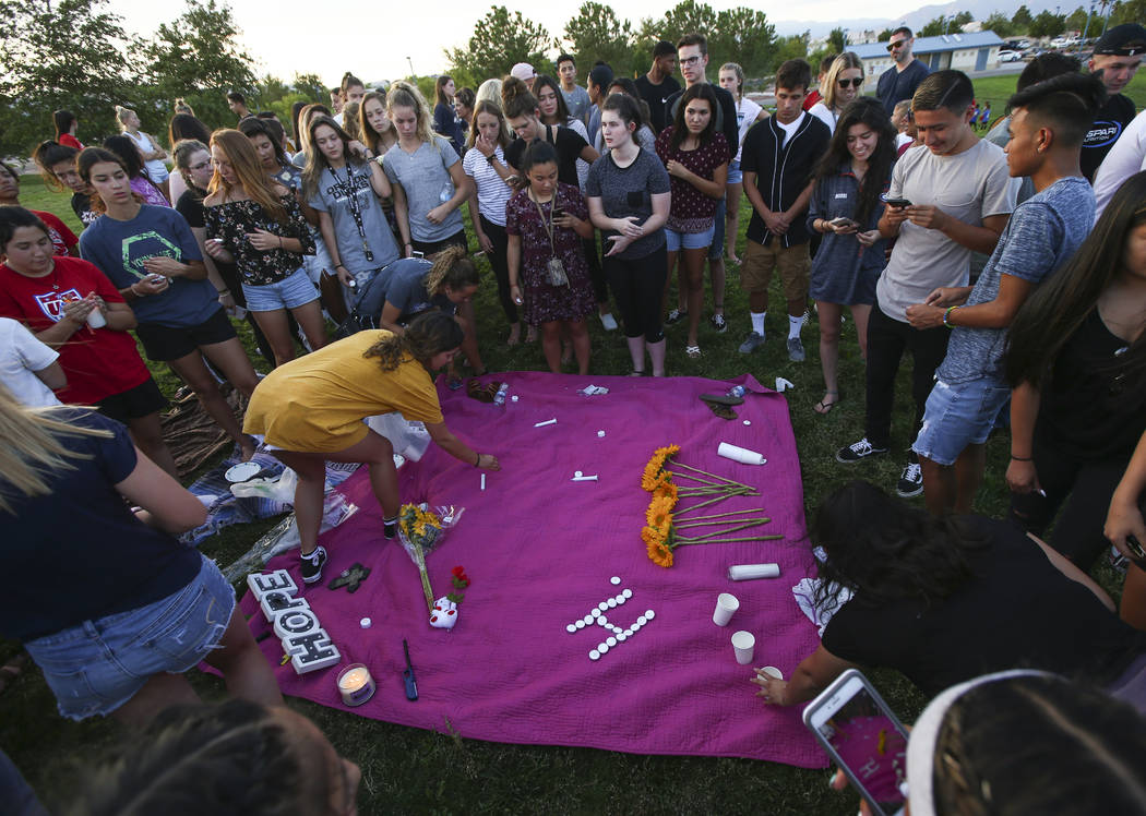 Savannah Day, left, in yellow, assists as people leave items behind during a vigil for Haylei Hughes, a former Cimarron-Memorial student-athlete, who died in a hiking accident in Wash., at Kellogg ...