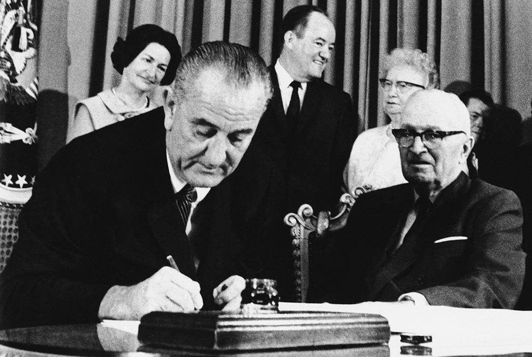 President Lyndon Johnson signs the Medicare Bill into law while former President Harry S. Truman, right, observes during a ceremony at the Truman Library in Independence, Mo., on July 30, 1965. At ...