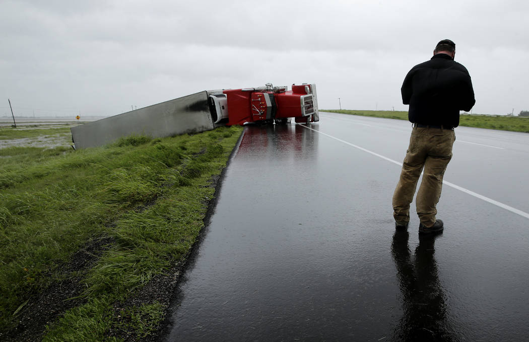 A passing motorist stops to look at a flipped truck in the aftermath of Hurricane Harvey Saturday, Aug. 26, 2017, north of Victoria, Texas. (AP Photo/Charlie Riedel)