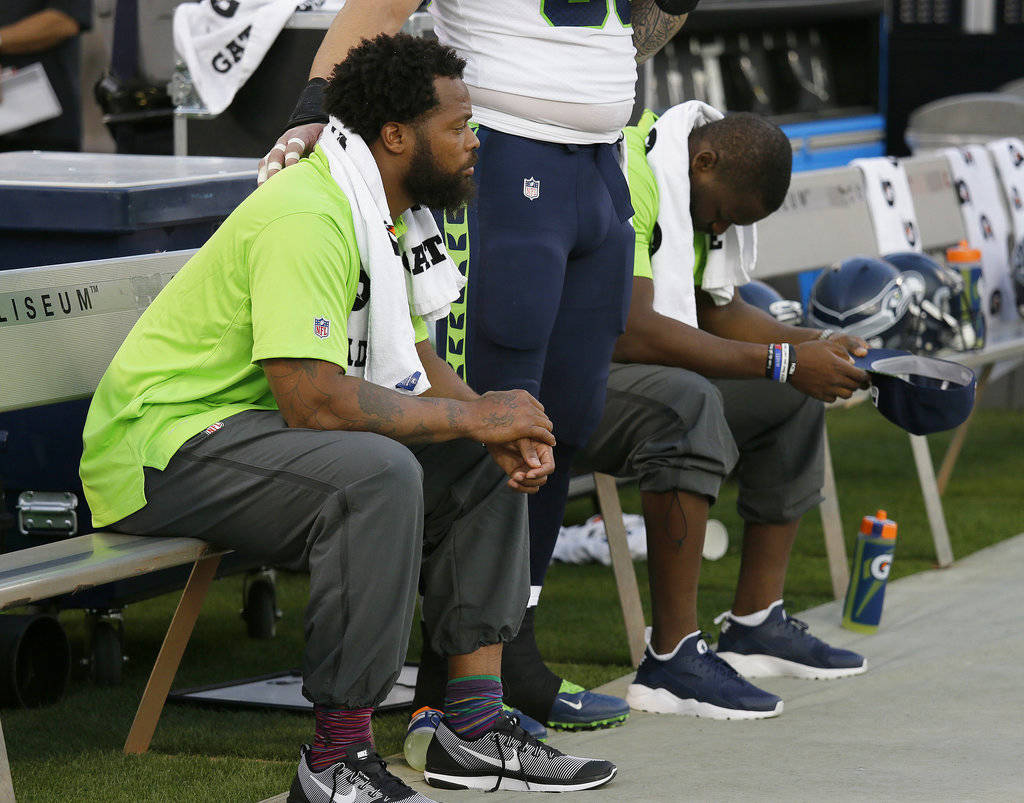 FILE - This Thursday, Aug. 31, 2017 file photo Seattle Seahawks defensive end Michael Bennett, left, sits during the playing of the national anthem next to Justin Britt, center, and another teamma ...