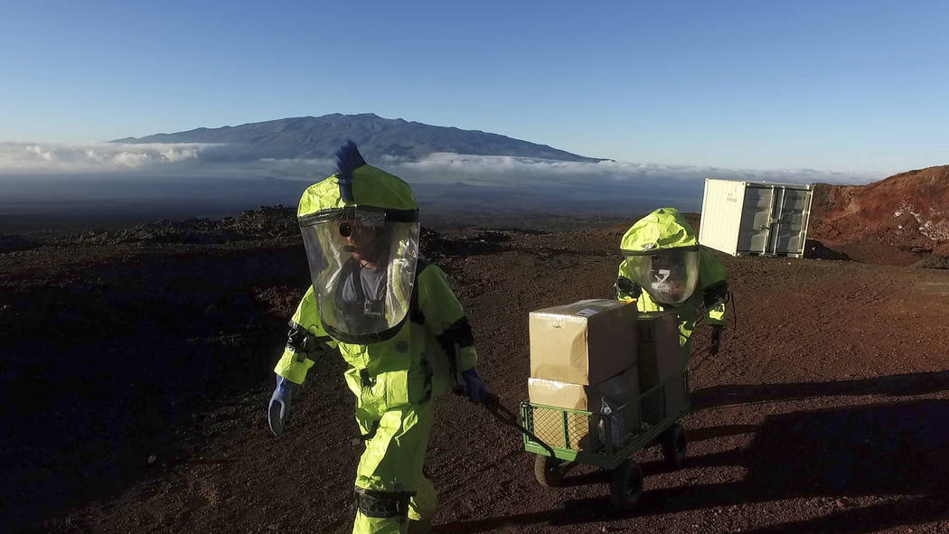 In this 2017 photo released by the University of Hawaii crew members of Mission V, walk up hill with a cart next to the university’s facility Hawaii Space Exploration Analog and Simulation (HI-S ...