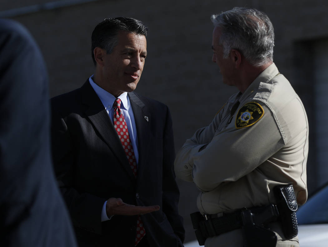 Gov. Brian Sandoval, left, and Clark County Sheriff Joe Lombardo talk while waiting for the arrival of President Donald Trump at McCarran International Airport in Las Vegas on Wednesday, Oct. 4, 2 ...