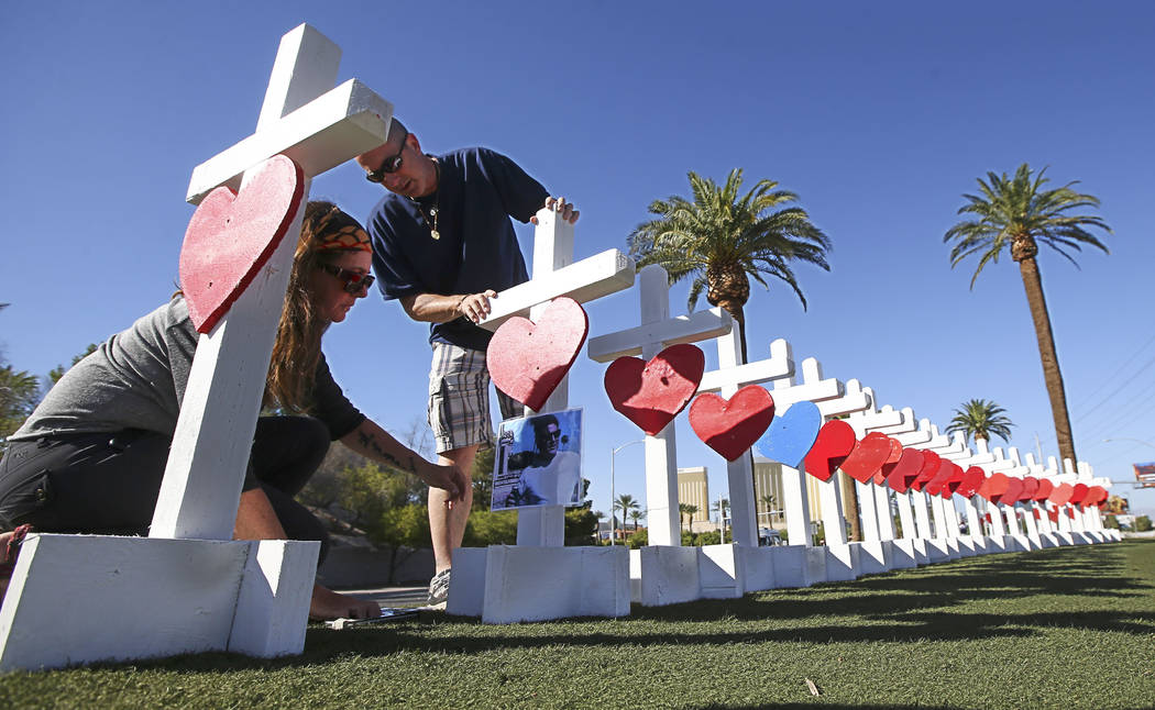 Sherri Camperchioli, left, and Jordan Cassel place photos of victims of Sunday's mass shooting on crosses left in their memory near the &quot;Welcome to Fabulous Las Vegas&quot; sign in La ...