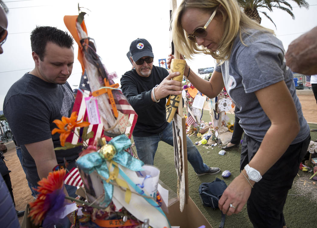 Chris Davis, center, and Mynda Smith, right, the father and sister of Route 91 shooting victim Neysa Tonks, gather items from Tonks' cross during a cross-moving ceremony at a memorial for the vict ...