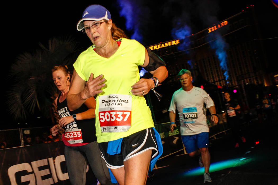 Cathy Hanehan of Saratoga Springs, center, crosses the finish line at the 10K run of the Rock 'n' Roll Las Vegas Marathon along the Strip near The Mirage in Las Vegas, Sunday, Nov. 12, 2017. Joel  ...