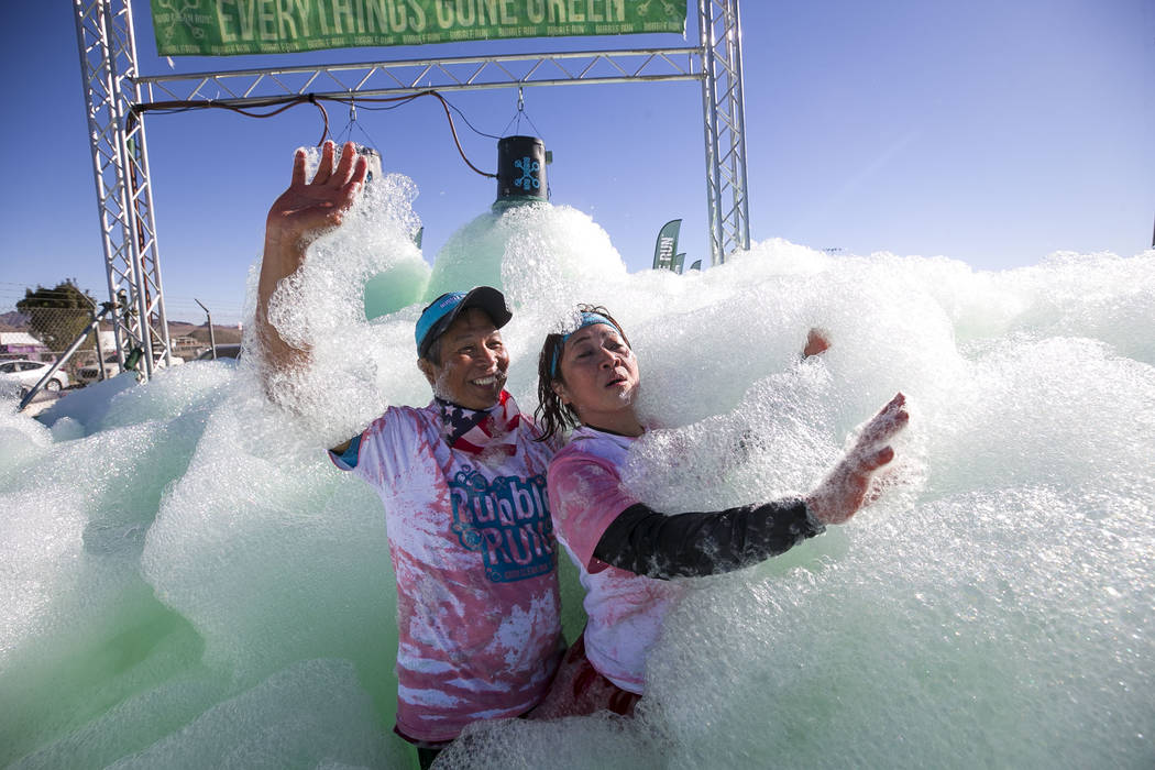 Las Vegas residents Conrad and Cristie Yabut run through a green foam sprayer during the Bubble Run 5K event at Sam Boyd Stadium in Las Vegas, Saturday, Nov. 18, 2017. Richard Brian Las Vegas Revi ...