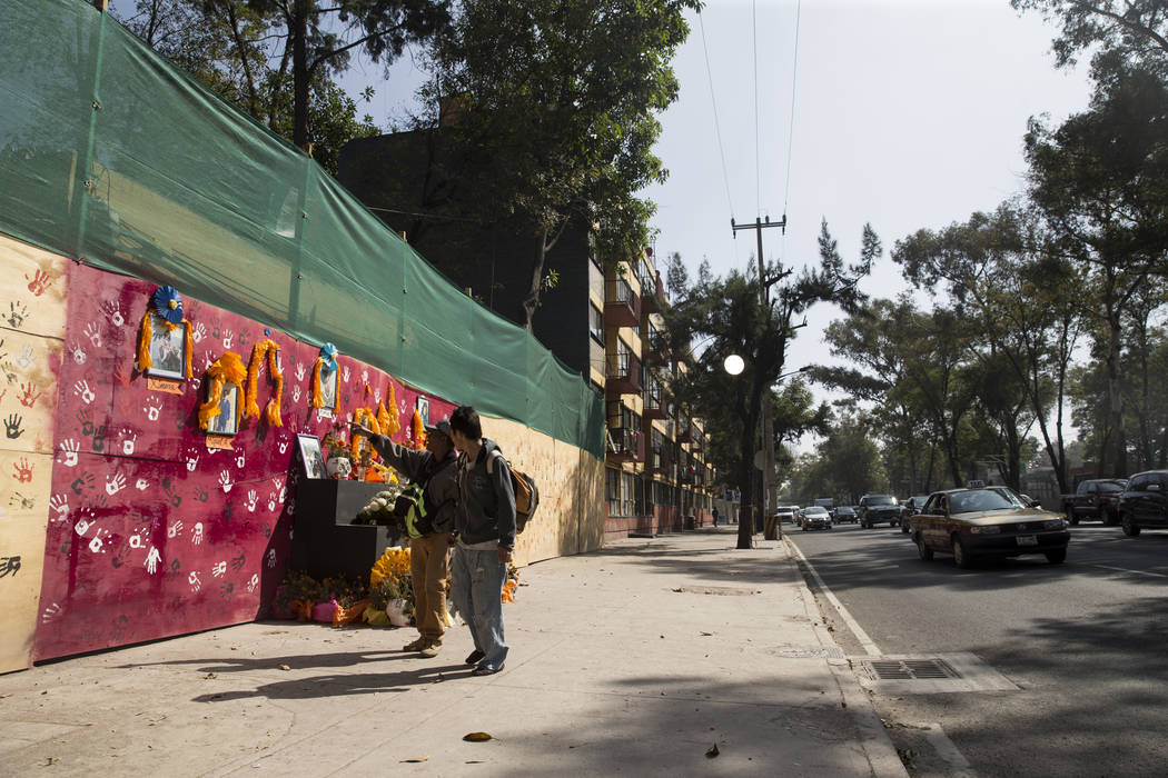 People walk next to a memorial for the victims who died after their apartment complex, Unidad Habitacional de Tlalpan, collapsed during the Sept. 19 earthquake in Mexico City, Mexico, Friday, Nov. ...