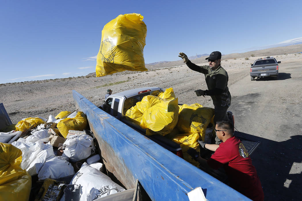 A Bureau of Land Management employee tosses a bag of trash into a roll-away dumpster during a volunteer cleanup hosted by the Bureau of Land Management at a popular target shooting area off South  ...