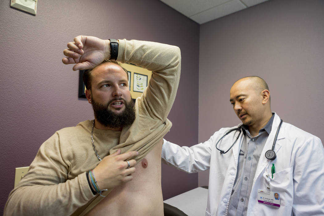 William King, left, holds up his arm while Dr. Edward S. Victoria examines King's bullet wound from the Route 91 Harvest festival shooting, in Dr. Victoria's clinic in Las Vegas, Thursday, Nov. 30 ...