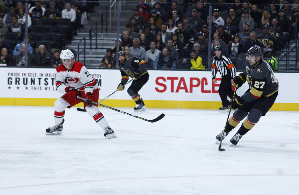 Vegas Golden Knights defenseman Shea Theodore (27) handles the puck as Carolina Hurricanes left wing Brock McGinn (23) prepares to defend during the first period of a NHL game in Las Vegas, Tuesda ...