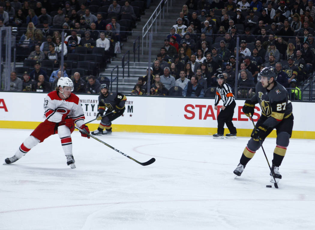 Vegas Golden Knights defenseman Shea Theodore (27) handles the puck as Carolina Hurricanes left wing Brock McGinn (23) prepares to defend during the first period of a NHL game in Las Vegas, Tuesda ...