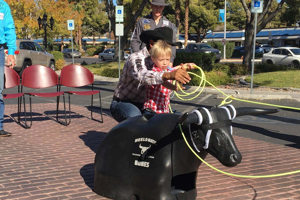 Four-year-old Tristan Duenez gets an assist from all-around world champion cowboy Junior Nogueira in roping a practice steer head Friday during an event partnering the Wrangler National Finals Rod ...