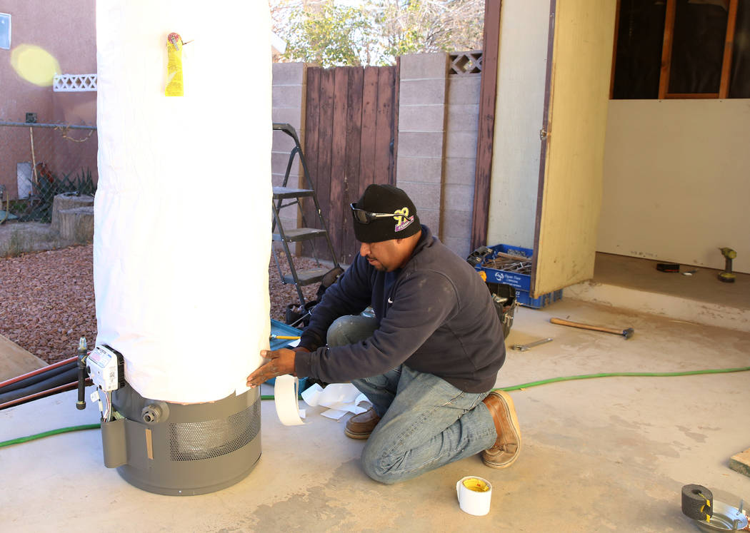 Abraham Gonzalez insulates a water heater outside the Las Vegas home of 87-year-old U.S. Air Force veteran Louise Jones Tuesday, Dec. 12, 2017. Rebuilding Together, a nationwide non-profit organiz ...