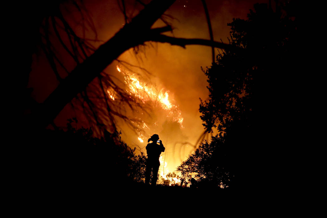 A firefighter takes a cell phone picture during a wildfire Saturday, Dec. 16, 2017, in Montecito, Calif. The so-called Thomas Fire is now the third-largest in California history. (Chris Carlson/AP)