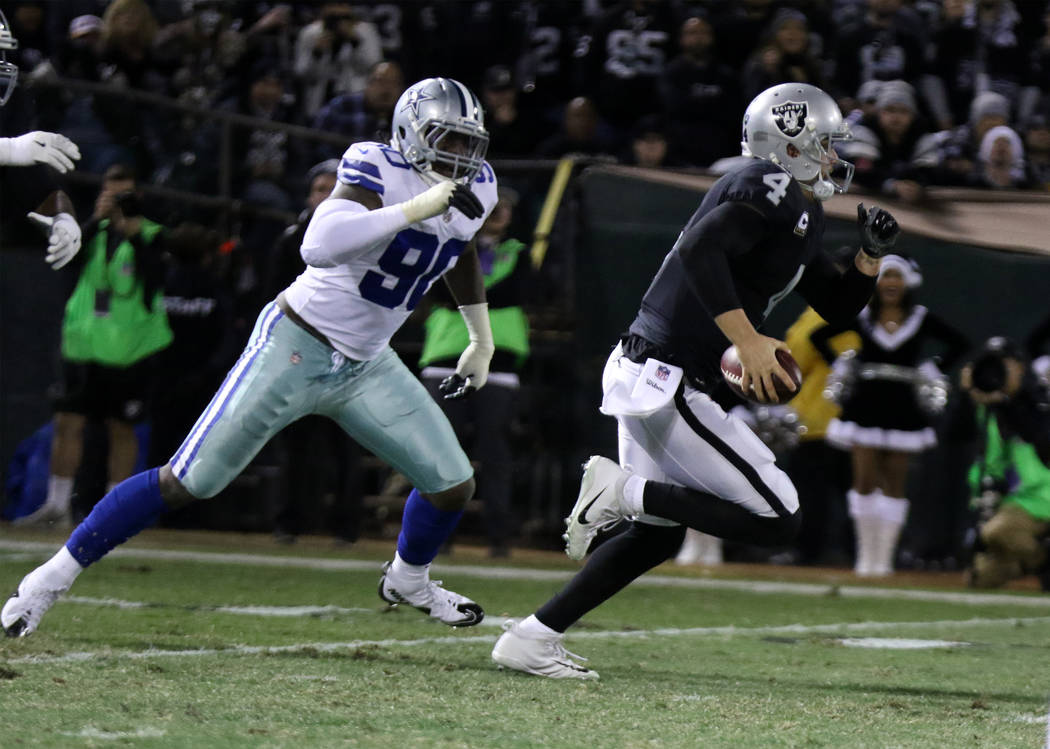 Oakland Raiders quarterback Derek Carr (4) scrambles with the football as Dallas Cowboys defensive end Demarcus Lawrence (90) closes in during the first half of a NFL game in Oakland, Calif., Sund ...