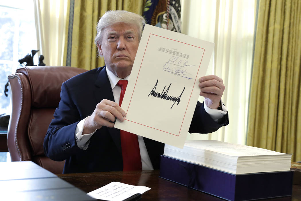 President Donald Trump displays the $1.5 trillion tax overhaul package he had just signed, Friday, Dec. 22, 2017, in the Oval Office of the White House in Washington. Trump touted the size of the  ...