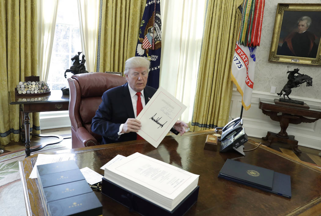 President Donald Trump displays the $1.5 trillion tax overhaul package he had just signed, Friday, Dec. 22, 2017, in the Oval Office of the White House in Washington. The bill provides generous ta ...