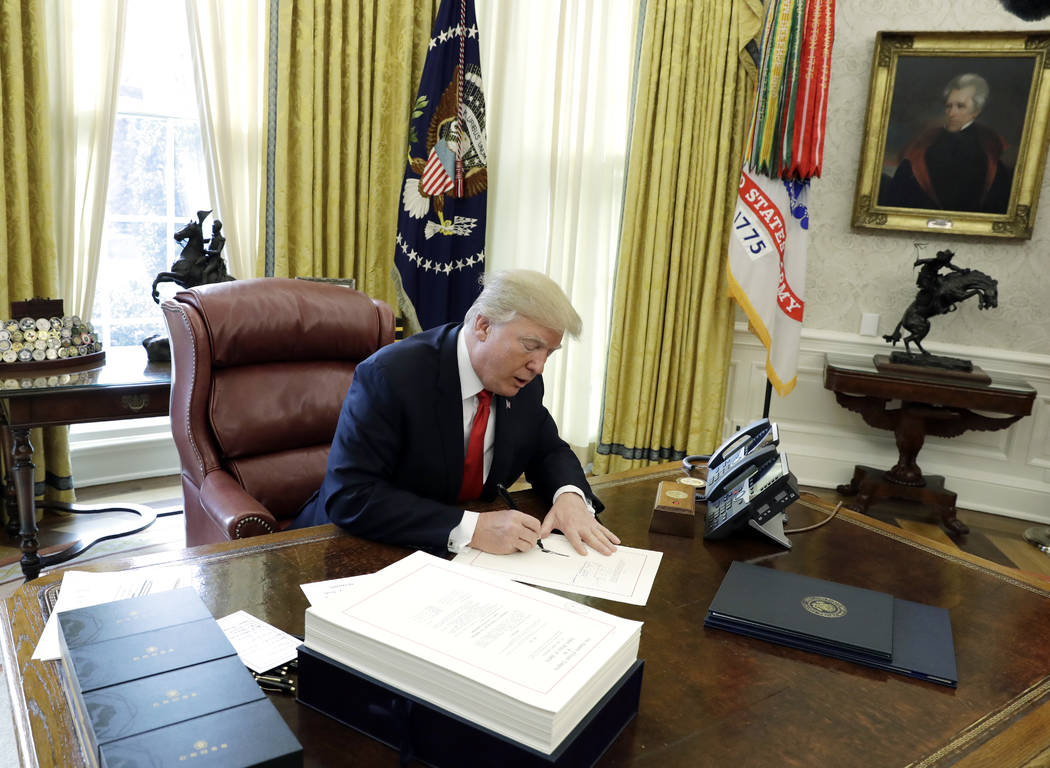 President Donald Trump signs into law a $1.5 trillion tax overhaul package, Friday, Dec. 22, 2017, in the Oval Office of the White House in Washington. Trump touted the size of the tax cut, declar ...
