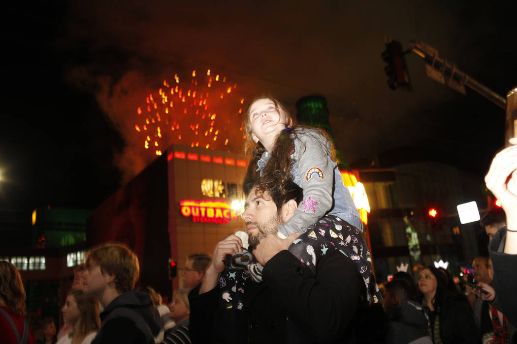 Paisley Tanabe, 8, sits on her father Miguel Alacala, 32, both of P[hoenix, Ariz., as fireworks go off along the Strip during the first minutes of New Year's Day in Las Vegas, Monday, Jan. 1, 2018 ...