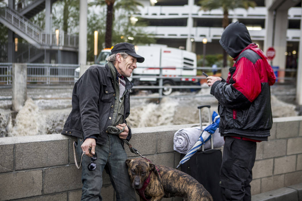 A man who identifies as "Motorcycle Dave" and another man, who declined to give his name, watch floodwaters rush by their makeshift home near The Linq Hotel in Las Vegas on Tuesday, Jan. 9, 2018.  ...
