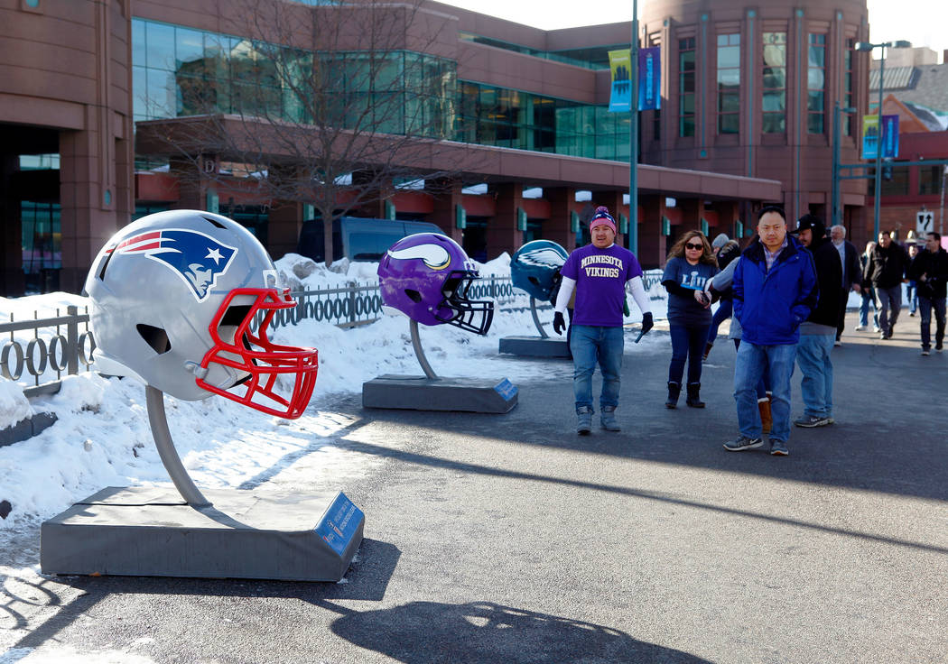 Fans check out the Philadelphia Eagles helmet, right, the New England Patriots helmet, left, and the Minnesota Vikings helmet as they head towards the NFL Experience at the Minneapolis Convention  ...