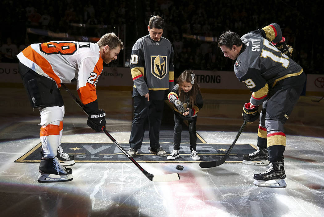 Hailey Dawson, center right, drops the puck for Philadelphia Flyers center Claude Giroux (28) and Vegas Golden Knights right wing Reilly Smith (19) before the start of an NHL hockey game between t ...