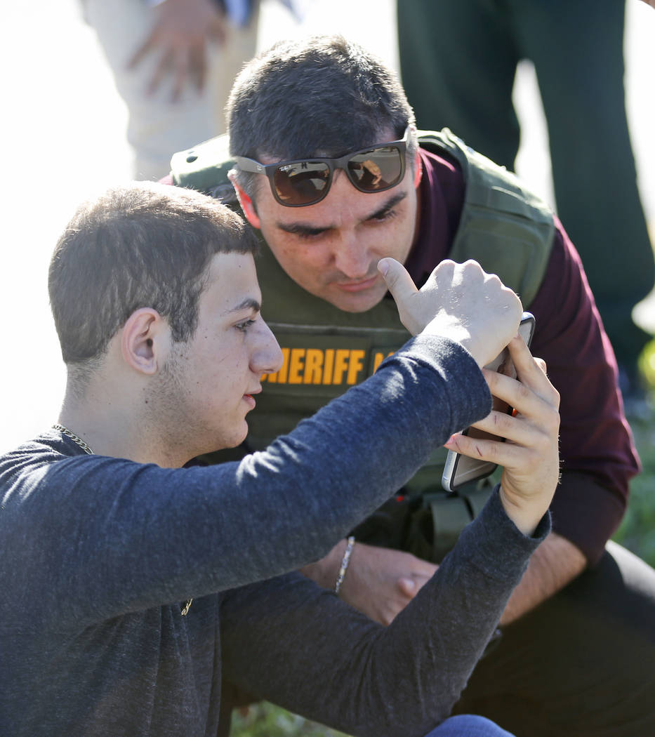 A student shows a law enforcement officer a photo or video from his phone, Wednesday, Feb. 14, 2018, in Parkland, Fla. A shooting at Marjory Stoneman Douglas High School sent students rushing into ...