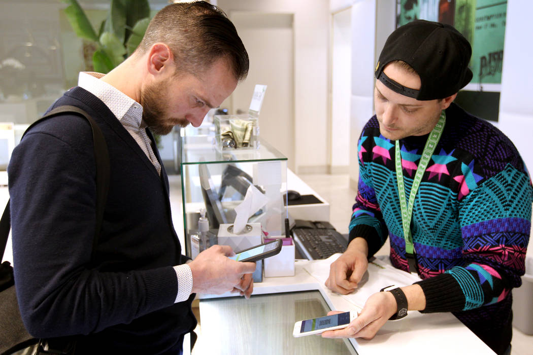 Gabriel Allred, co-founder of Tokes Platform, left, scans a QR bar code to use his cryptocurrency to make a purchase with budtender Patrick Murphy at Pisos dispensary, at 4110 S. Maryland Pkwy. in ...