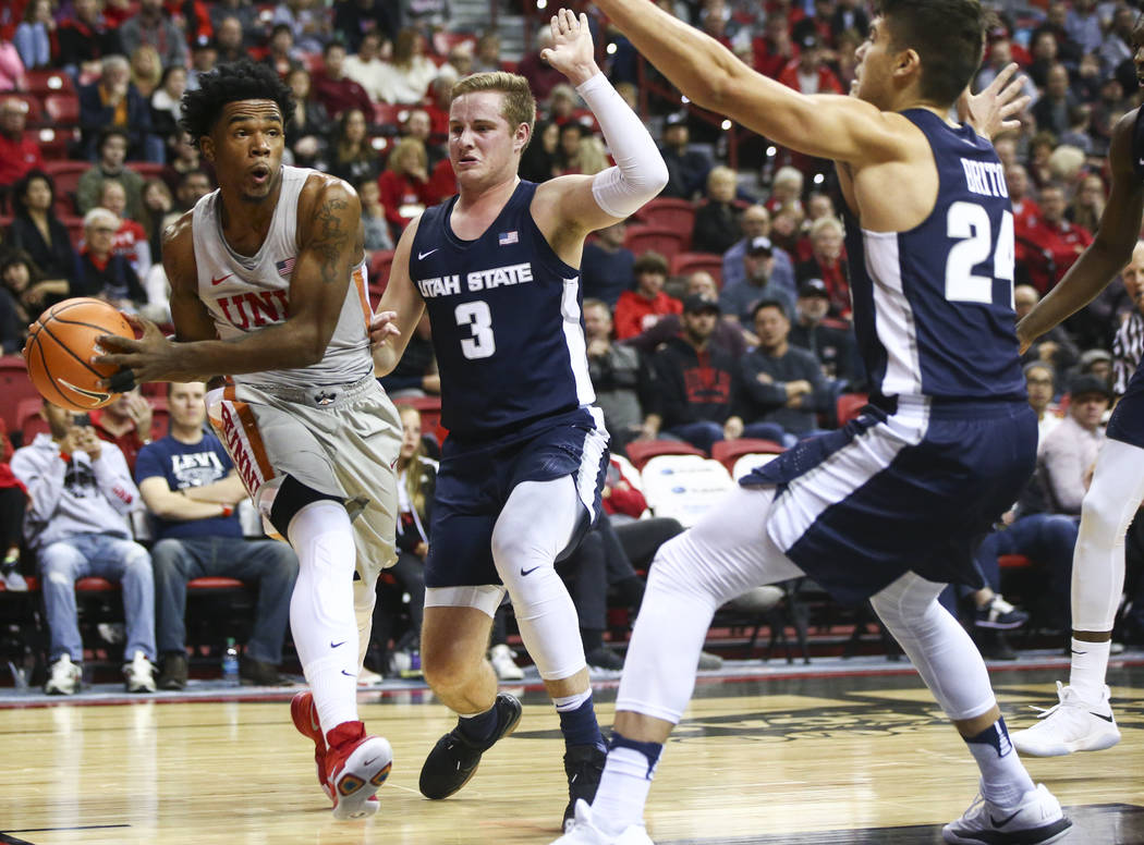 UNLV Rebels guard Jovan Mooring (30) looks to pass as Utah State Aggies guards Sam Merrill (3) and Diogo Brito (24) defend during the first half of a basketball game at the Thomas & Mack Cente ...