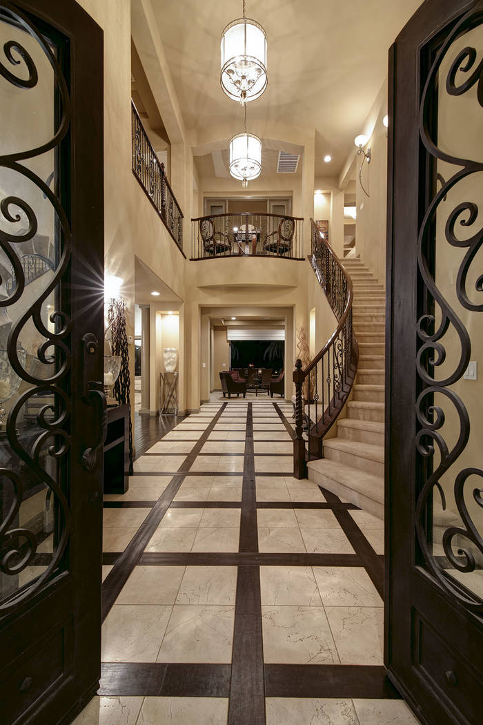 Its grand, wooden double-door entry opens into an expansive foyer with travertine flooring framed by wood accents. (Synergy/Sotheby’s International Realty)