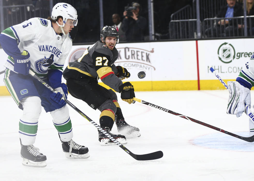 Golden Knights defenseman Shea Theodore (27) eyes the puck as it flies past Vancouver Canucks defenseman Derrick Pouliot (5) during the first period of an NHL hockey game at T-Mobile Arena in Las  ...