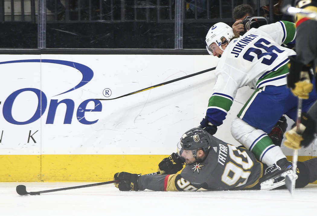 Golden Knights left wing Tomas Tatar (90) tries to keep control of the puck as he falls to the ice as Vancouver Canucks left wing Jussi Jokinen (36) defends during the third period of an NHL hocke ...