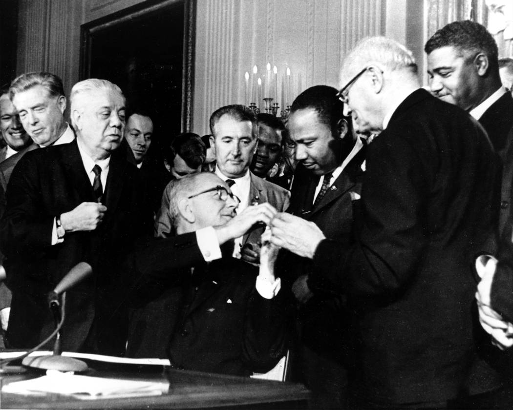 U.S. President Lyndon B. Johnson reaches to shake hands with Dr. Martin Luther King Jr. after presenting the civil rights leader with one of the 72 pens used to sign the Civil Rights Act of 1964 i ...