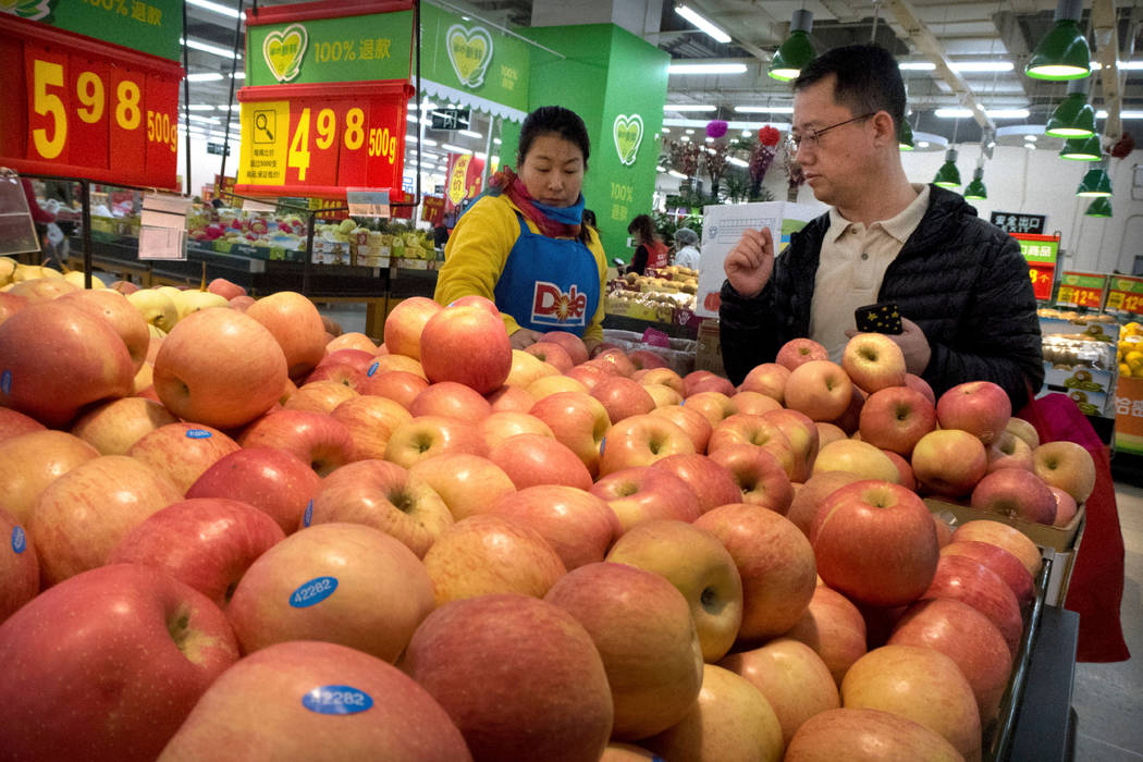 A woman wearing a uniform with the logo of an American produce company helps a customer shop for apples a supermarket in Beijing. China raised import duties on a $3 billion list of U.S. pork, frui ...