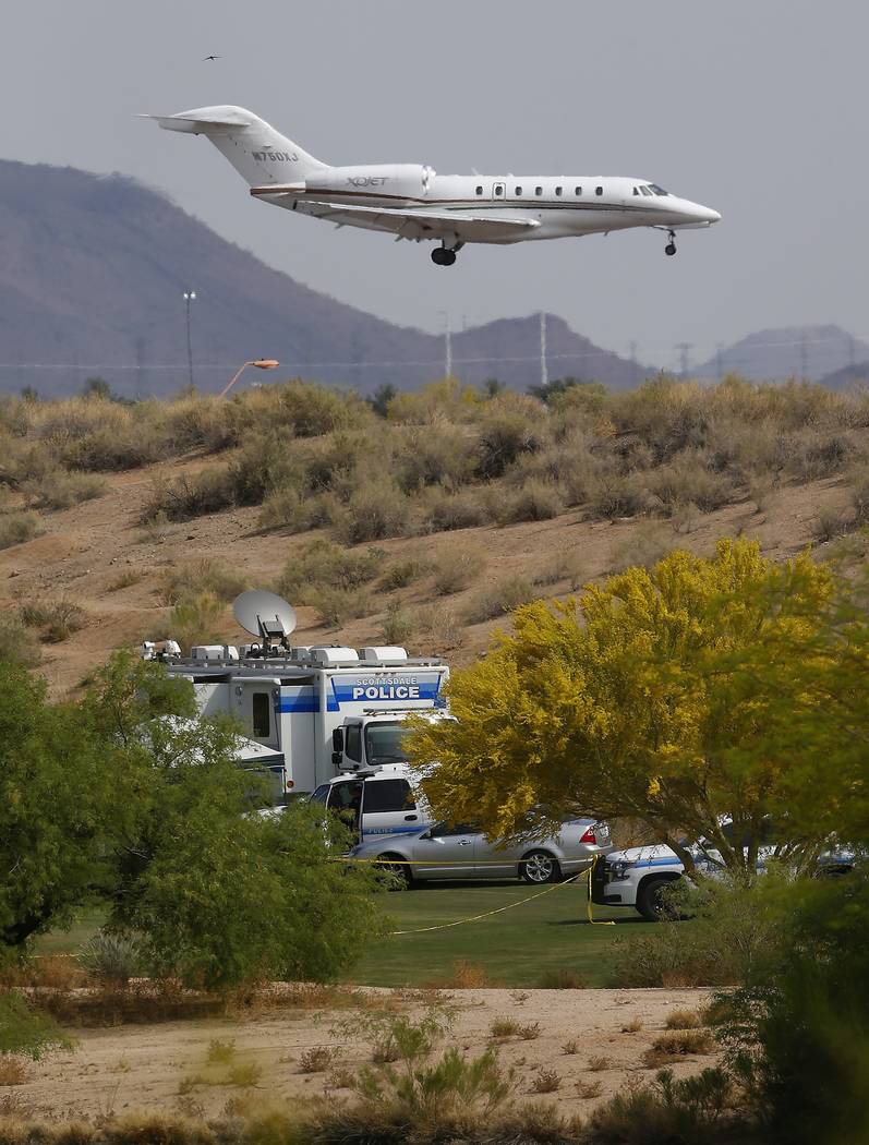 As a jet comes in for a landing at Scottsdale Airport, authorities park on a golf course near the site of a plane crash that killed several people Tuesday, April 10, 2018, in Scottsdale, Ariz. (AP ...