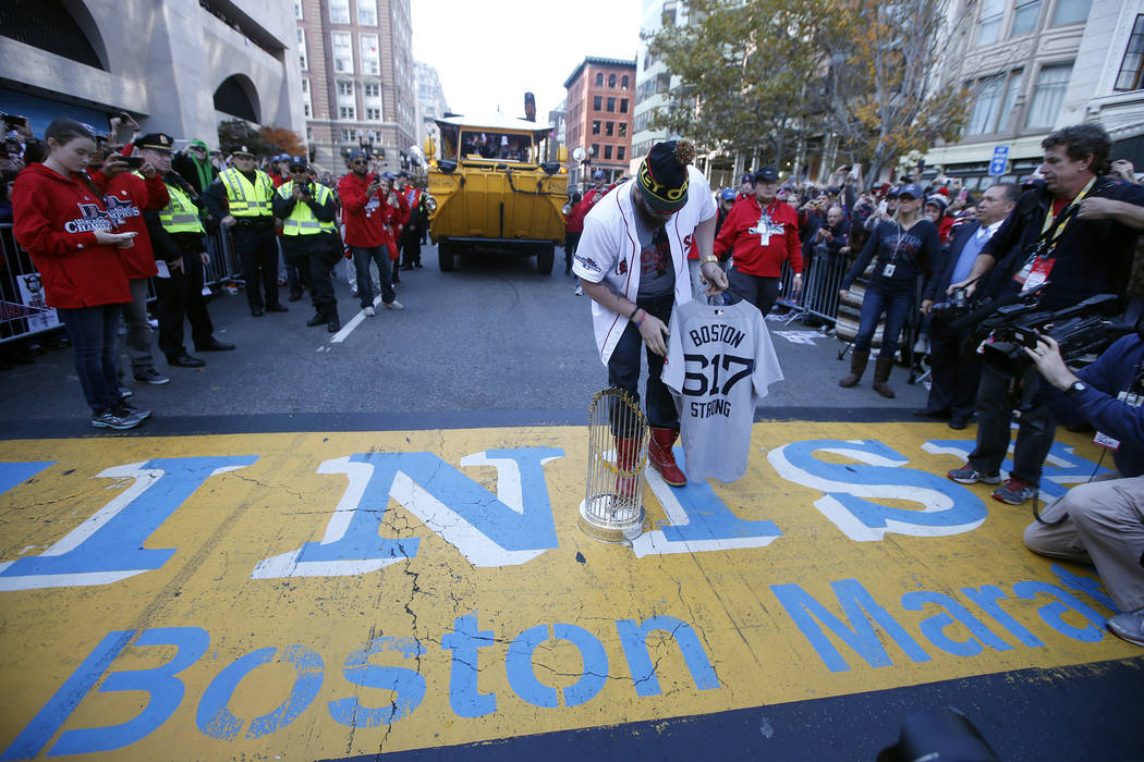 Boston Red Sox's Jonny Gomes places the championship trophy and a Red Sox baseball jersey at the Boston Marathon Finish Line during a pause in their World Series victory rolling rally in Boston, S ...