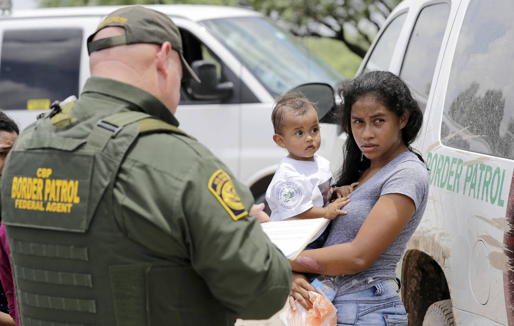 A mother migrating from Honduras holds her 1-year-old child while surrendering to U.S. Border Patrol agents after illegally crossing the border Monday, June 25, 2018, near McAllen, Texas. (AP Phot ...