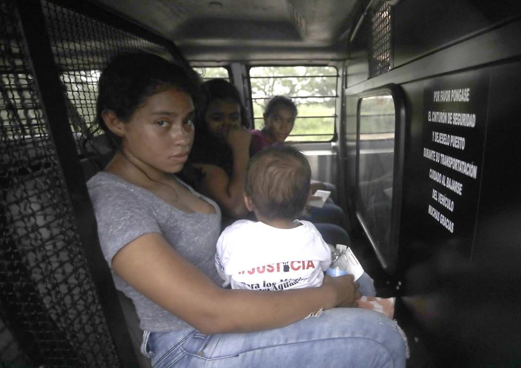 A mother migrating from Honduras holds her one-year-old child in the back of a transport van after surrendering to U.S. Border Patrol agents Monday, June 25, 2018, near McAllen, Texas. They are pa ...