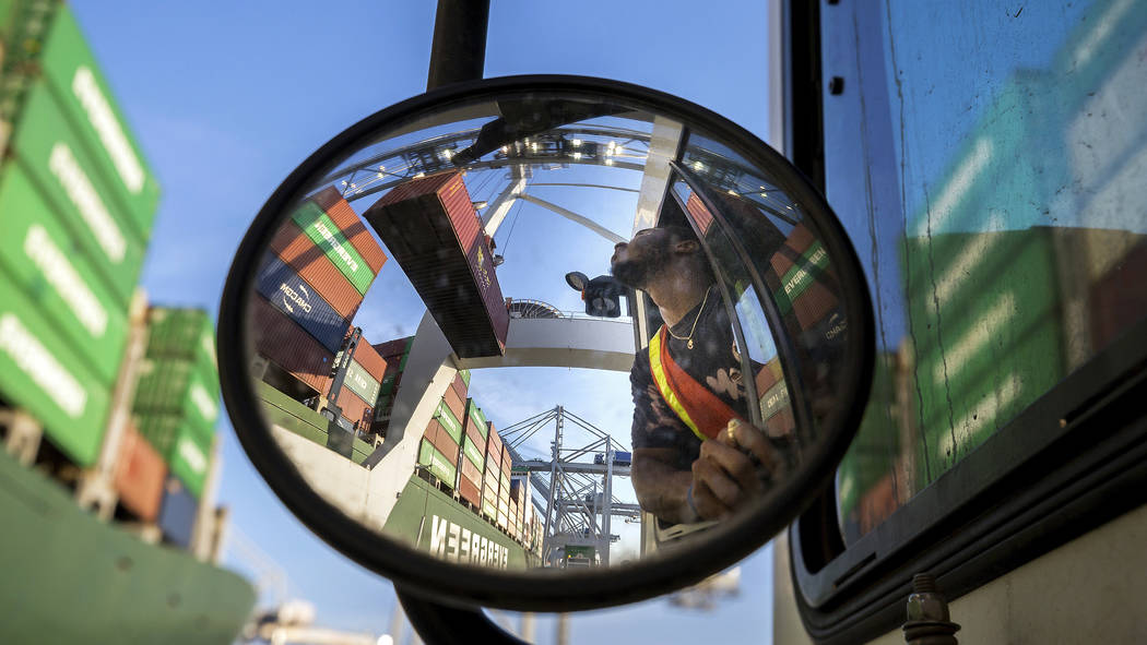 In this June, 19, 2018 photo, a jockey truck driver waits for his load of a shipping container to clear his trailer as a shore crane lifts the 40-foot onto the container vessel Ever Linking at the ...