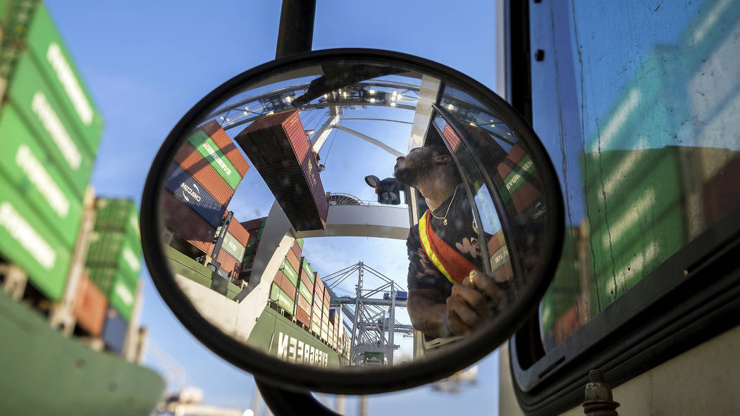 In this June, 19, 2018 photo, a jockey truck driver waits for his load of a shipping container to clear his trailer as a shore crane lifts the 40-foot onto the container vessel Ever Linking at the ...
