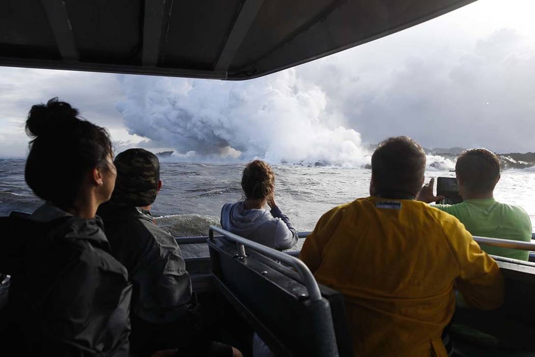 In this May 20, 2018 file photo, people watch a plume of steam as lava enters the ocean near Pahoa, Hawaii. Officials say an explosion sent lava flying through the roof of a tour boat off the Big ...