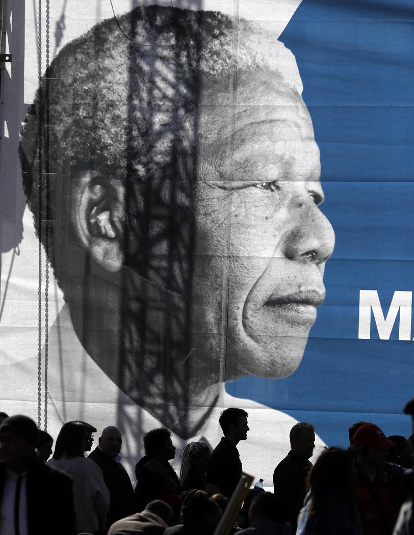 People gather below a giant banner of the late Nelson Mandela as they wait for the 16th Annual Nelson Mandela Lecture by former President Barack Obama at the Wanderers Stadium in Johannesburg, Sou ...