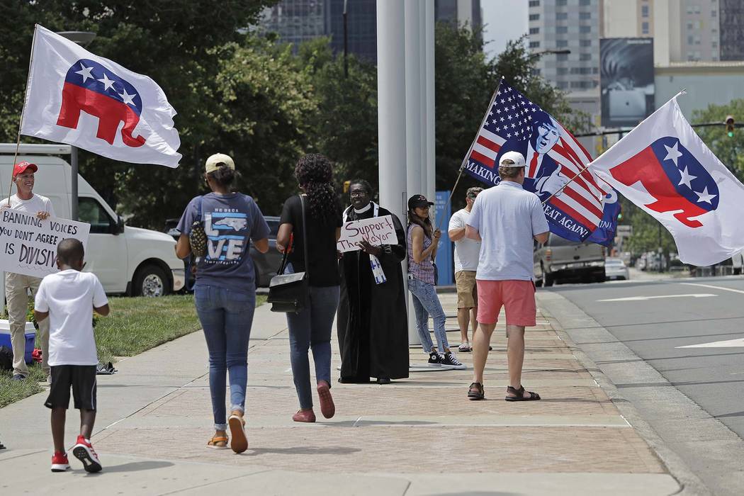People walk past a group of Trump and RNC supporters outside city hall during a public forum before the Charlotte City Council votes whether to host the 2020 Republican National Convention at a me ...