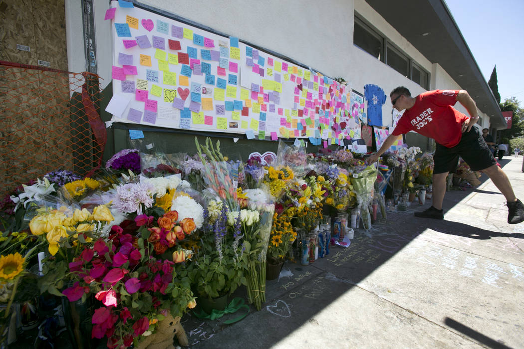 A Trader Joe's employee from the Cerritos, Calif., store pauses at a makeshift memorial of flowers, candles and notes growing on the sidewalk outside the Silver Lake Trader Joe's store in Los Ange ...