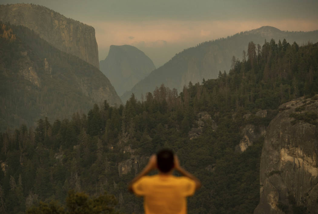 Francisco Avendano, visiting from Madrid, Spain, photographs Half Dome as smoke from the Ferguson Fire hangs over Yosemite National Park, Calif., on Tuesday, July 24, 2018. Parts of the park, incl ...
