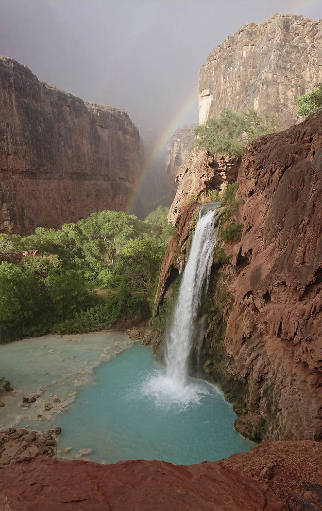 This Wednesday, July 11, 2018 photo released by Benji Xie shows a rainbow over a waterfall on the Havasupai reservation in Supai, Ariz. About 200 tourists were being evacuated Thursday from a camp ...
