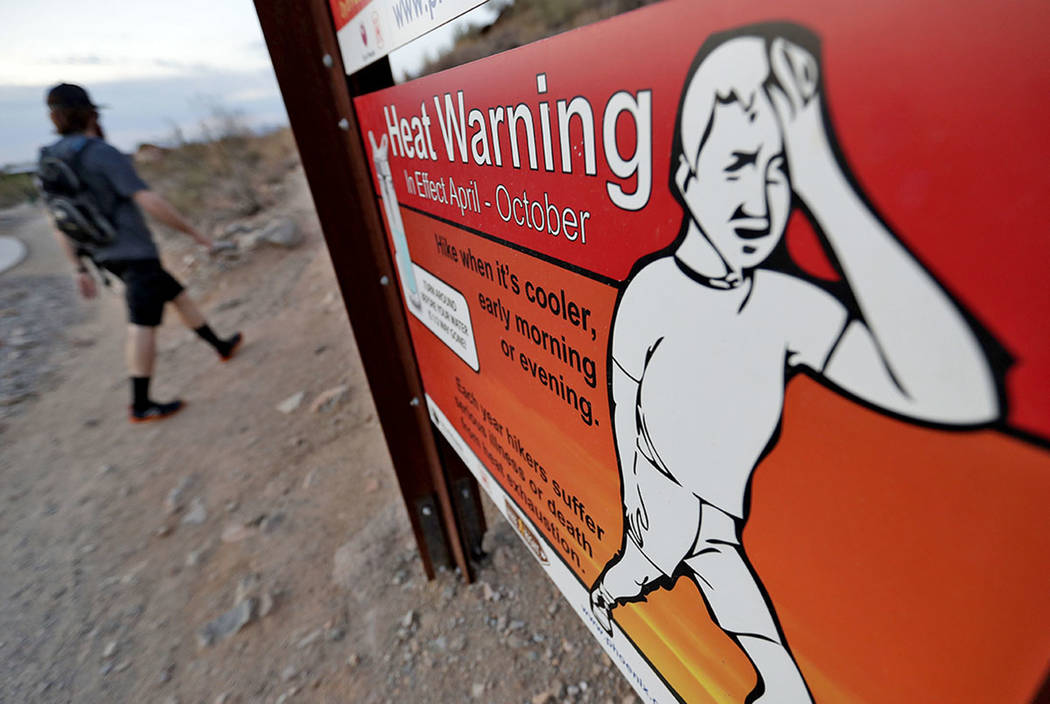 In this Tuesday, July 24, 2018 photo, a hiker walks past a heat warning sign at sunrise, in Phoenix. (AP Photo/Matt York)
