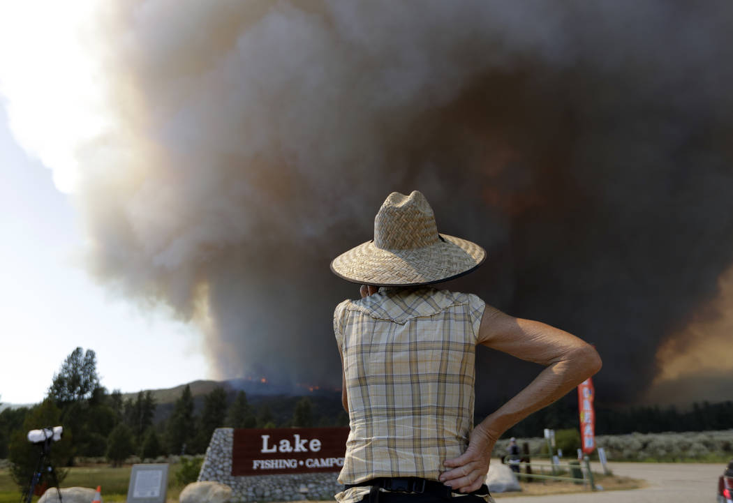 A woman watches a plume of smoke from a wildfire Thursday, July 26, 2018, in Mountain Center, Calif. A fast-moving wildfire, believed to have been sparked by arson, tore through trees, burned home ...